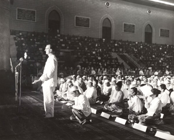 Addressing the sixth Buddhist Synod. A European man stands before a microphone, addressing a