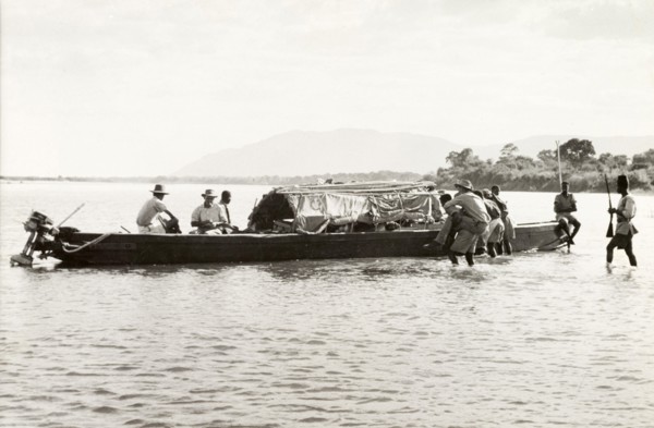 Boarding the District Commissioner's River boat. A European man is carried through shallow water to