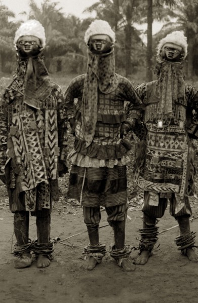 Juju practitioners. Three juju dancers in costume wear wooden masks on top of their heads, ornate