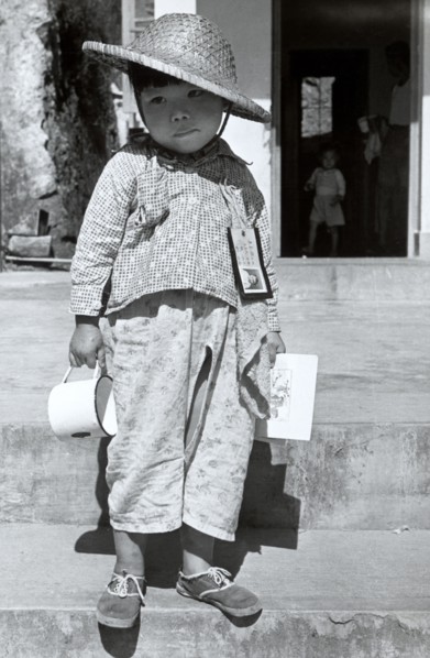 Refugee from China. A refugee boy from China stands on steps infront of an open doorway with an