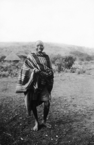 Kamba boy. Informal portrait of a smiling Kamba boy wearing a striped blanket. Kenya, circa 1927.