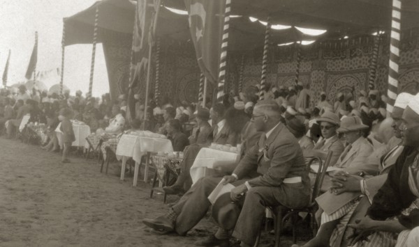 Kings' Day celebrations. A large, mostly male, crowd of onlookers sit around tables beneath a