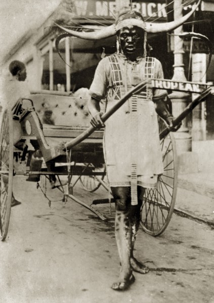 Rickshaw puller in Pietermaritzberg. A rickshaw puller stands between the shafts of his empty