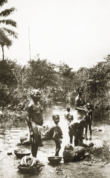 River laundry. A group of half-naked African women and children wash clothes in a shallow river