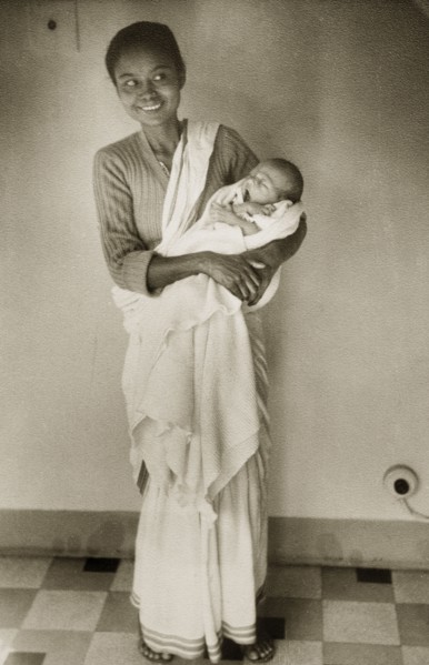 An Indian ayah with infant. Dressed in a flowing sari, an smiling Indian ayah (nursemaid) holds a