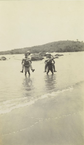 Out of water. Two European men wearing solatopi hats are carried above the water on the backs of