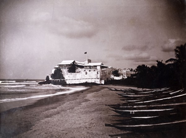 Christiansborg castle, Gold Coast. A line of canoes sit on a beach in front of Christiansborg