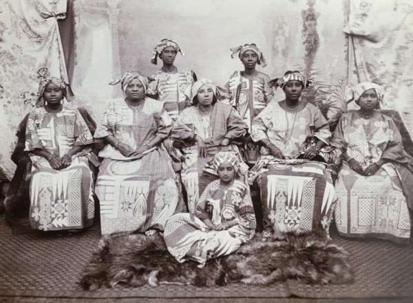 Eight women in indigo dresses. The women wear tailored gowns of dark cloth (probably indigo blue