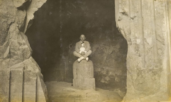 Inside the Elephanta Caves. A European man sits cross-legged, posing for the camera on a stone