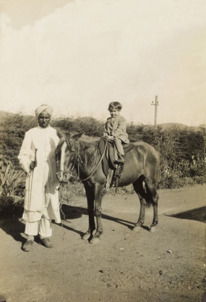 An Indian 'syce'. An Indian 'syce' (hostler) guides a pony ridden by a young British child along a