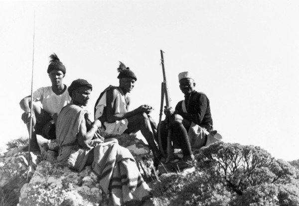 Kikuyu Home Guards on patrol. Four Kikuyu Home Guards on patrol sit atop a rocky outcrop. One wears