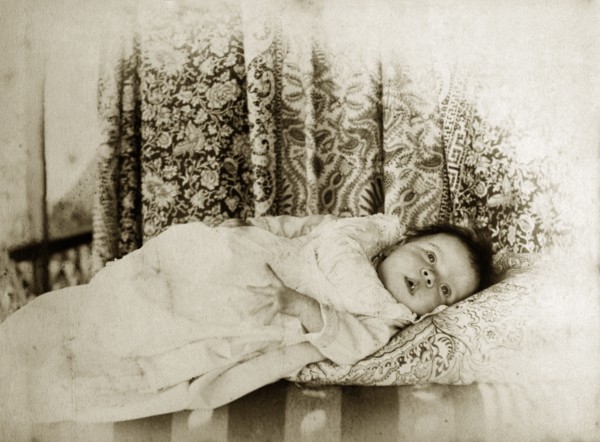 Portrait of a baby, Australia. A young baby dressed in a white gown gazes curiously into the