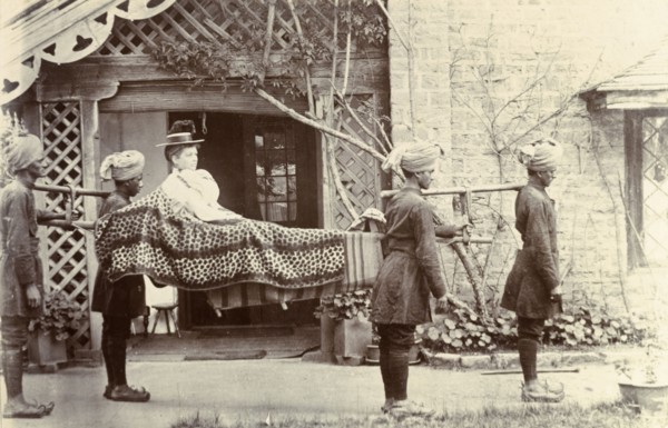 Mem Sahib Blount goes visiting. Mem Sahib Blount reclines in an open sedan chair as she is carried