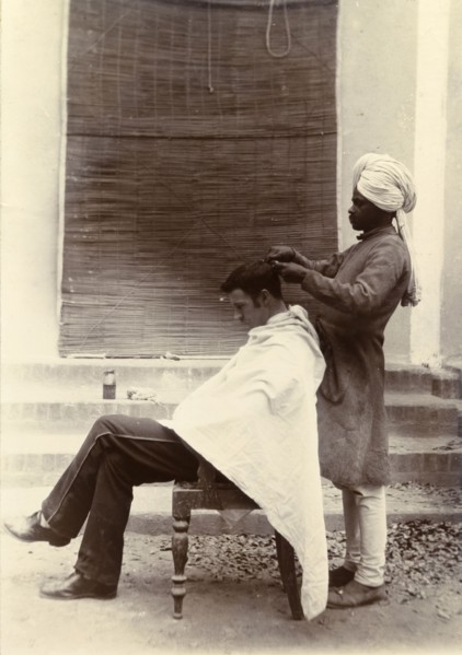 Cut your hair Sir'. A turbaned Indian barber trims the hair of a British gentleman who sits