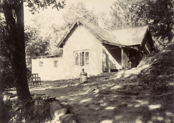 Mrs Page reads in the garden. A distant figure identified as 'Mrs Page' sits reading her book in