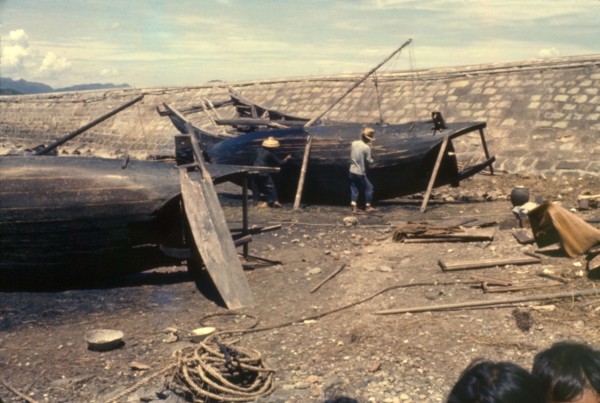 Re-caulking a sampan. Fishermen re-caulk the upturned bottoms of their sampans, filling in the
