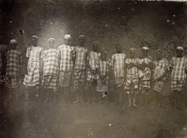 Convicts, Uganda, 1906. Group portrait of men wearing a uniform of checked cloth and ankle chains.