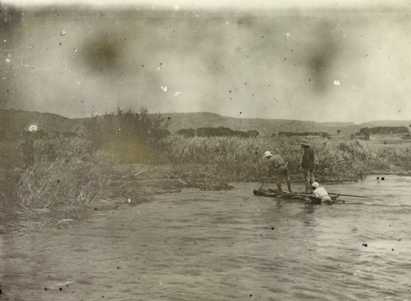 Coming ashore at Lake Victoria. A tiny wooden vessel is brought ashore by three African men on the