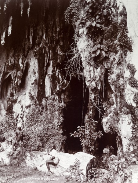 Entrance to the Batu Caves. Two Tamil men sit outside the entrance to the Batu caves in the jungle.