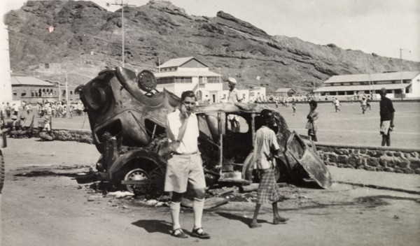 Vehicles destroyed during Arab riots in Aden, 1947. A European man stands by the burnt out shells