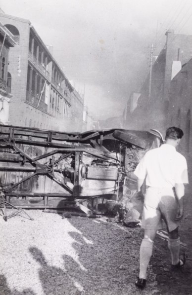 Aftermath of Arab riots in Aden, 1947. A European man walks around an upturned truck lying in the