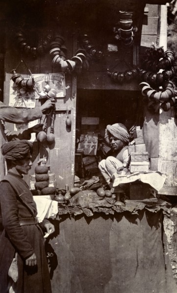 Roadside stall at Mussoorie bazaar. An Indian man sits hunched up on a roadside stall in a bazaar