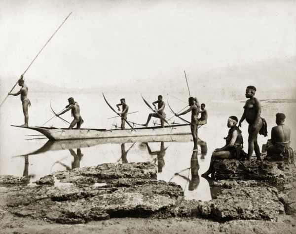 Andaman Islanders fishing. Six nearly naked men stand in a canoe, or in shallow water beside it,