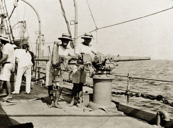 A gun on RIMS 'Minto'. British naval officers pose, leaning on a three pound gun on the deck of