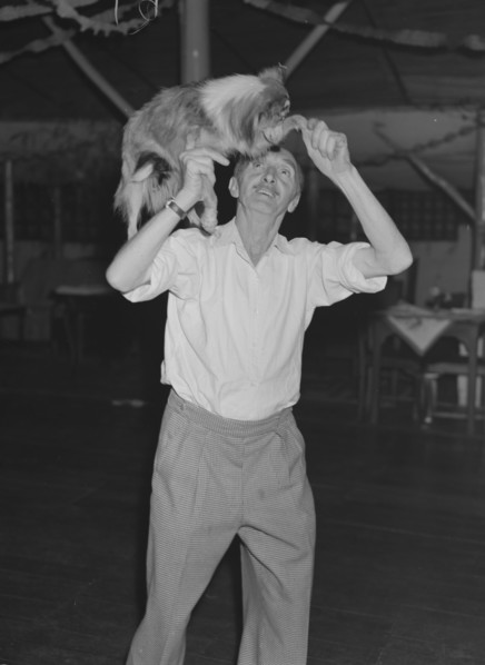 Tom dances with a dog. A man identified as 'Tom', lifts a worried-looking collie dog onto his