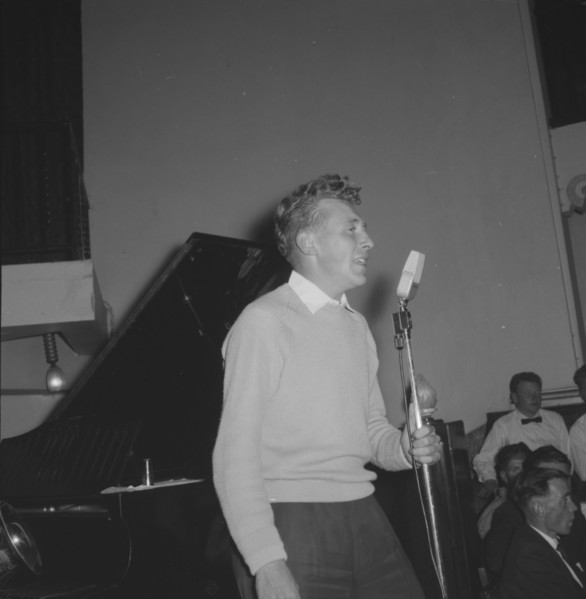 Jazz Ball singer. A casually dressed singer, supported by a band, clutches an upright microphone as