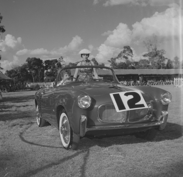 Number 12 on parade. A couple sit inside an open-top car marked with the number 12 at a vehicle
