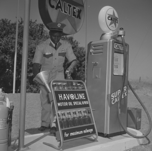 Havoline at Caltex. A uniformed attendant holds a funnel in one hand and a bottle of 'Havoline