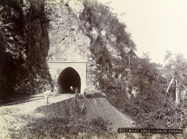 Mountainside tunnel, Jamaica. Three men stand at the entrance to a railway tunnel cut into the side