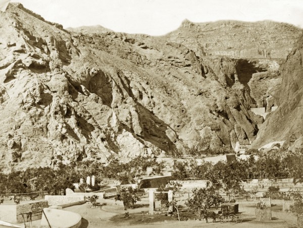 Water wells, Aden. Steep mountains rise up immediately behind several masonry wells, which are