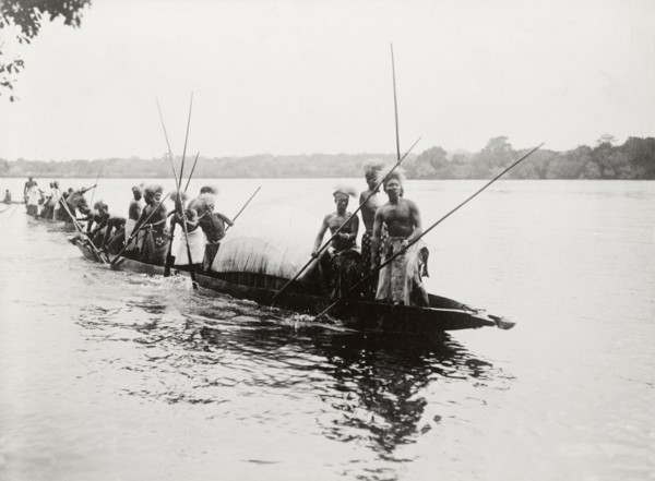 Canoes near Kandahar Island. A group of semi-naked men wearing traditional dress and headgear,