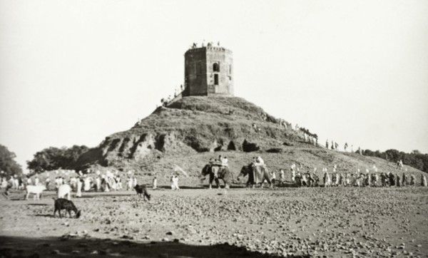 Monument near Benares. A long line of people, some riding elephants, visit an unidentified monument