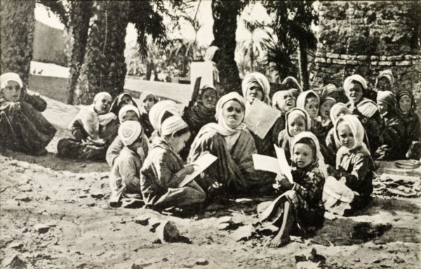 Outdoors school, Egypt. A group of young children sit cross-legged on a patch of desert sand as