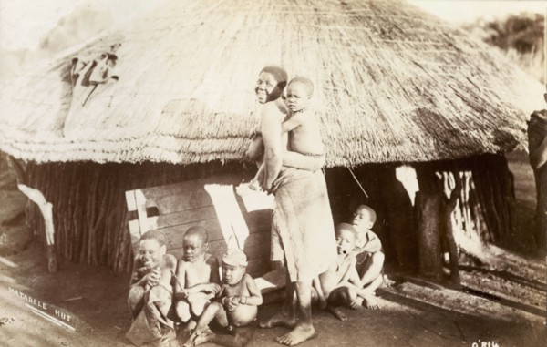 A Matabele family. A Matabele (Ndebele) woman turns to smile for the camera, a young child clinging