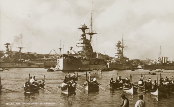 The Grand Fleet at Malta. Several small luzzus (row boats) share a Maltese harbour with two huge
