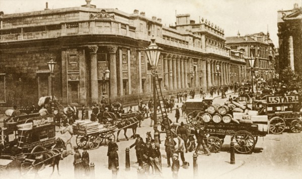 Outside the Bank of England. Horse-drawn carriages and pedestrians bustle about on a street running