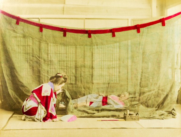 Japanese sleeping arrangements. A kneeling Japanese woman dressed in a kimono lifts the corner of a