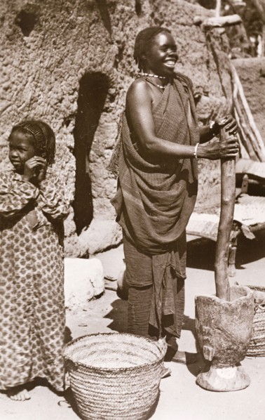 Grinding 'durra', Sudan. A Sudanese woman in traditional dress smiles as she uses a large pestle