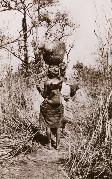 How women travel in the Sudan'. Two Sudanese women in traditional dress walk along an overgrown