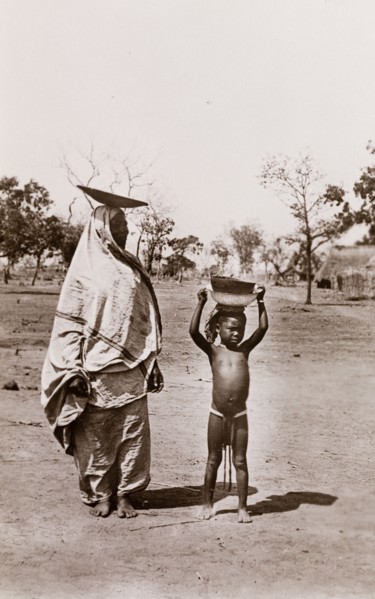 Mother and child carrying bowls. A mother and her child carry bowls on their heads along a village