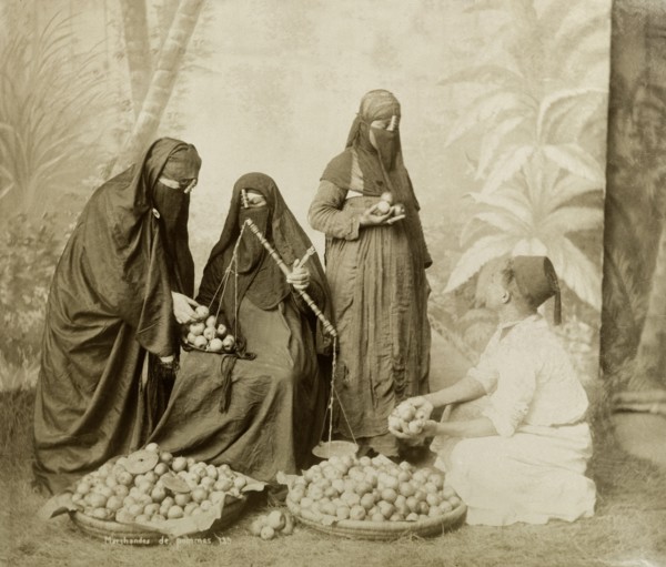 North African apple seller. Posed studio portrait of a man wearing a fez selling apples to three