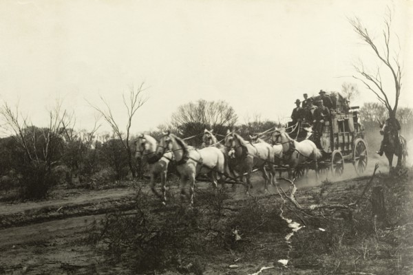 Stage coach travel in the outback. Six horses pull a stage coach full of people along a dirt track