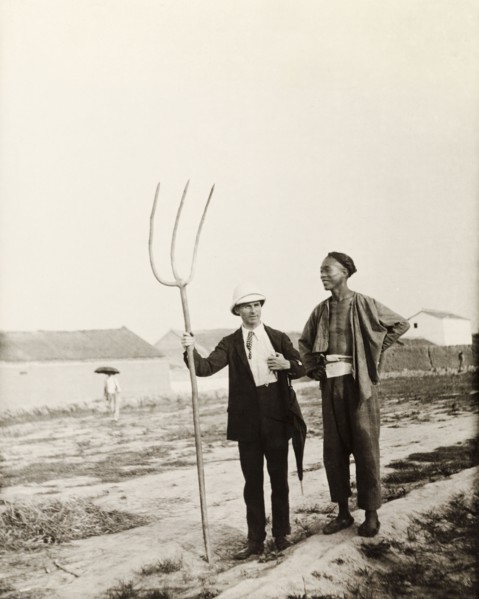 European man with Chinese farming tool. A European man, dressed in a suit and solatopi hat, holds a