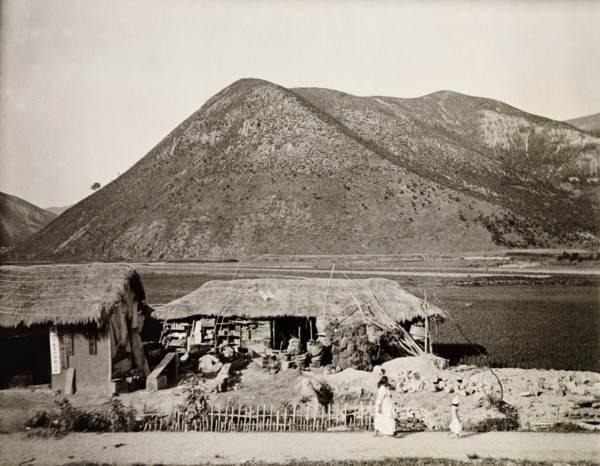 Dwelling in the mountains, Korea. A small dwelling with a thatched roof sits at the edge of a flat