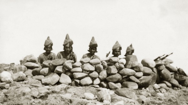 Five frontier guards. Five armed guards, dressed in uniforms and turbans, peer over the top of a
