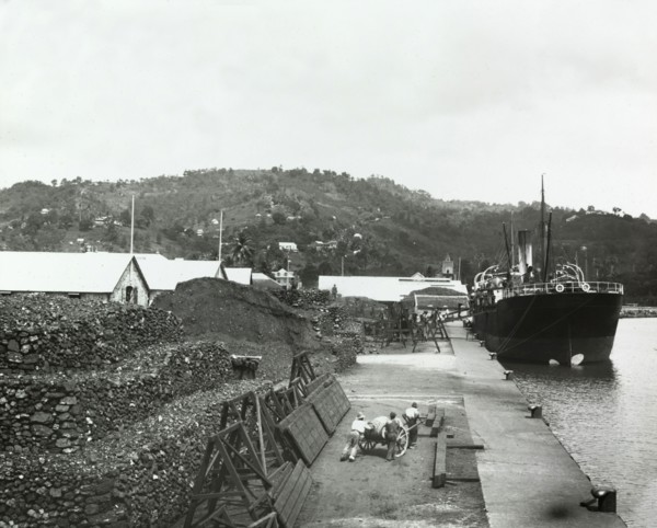 Unloading a cargo in St Lucia. A line of porters, carrying baskets on their heads, unload cargo